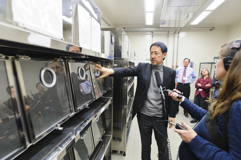 Researcher, Kawaoka points to a metal and glass holding tank as hands holding microphones are seen