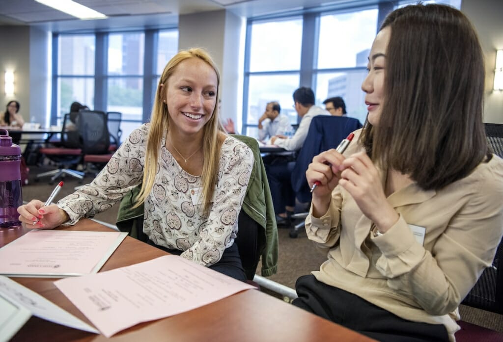 two women smiling at each other while sitting at a table