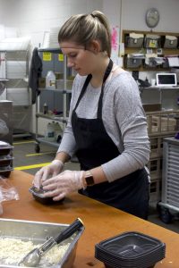 Woman in hairnet, apron, plastic cloves seen applying cover to food container