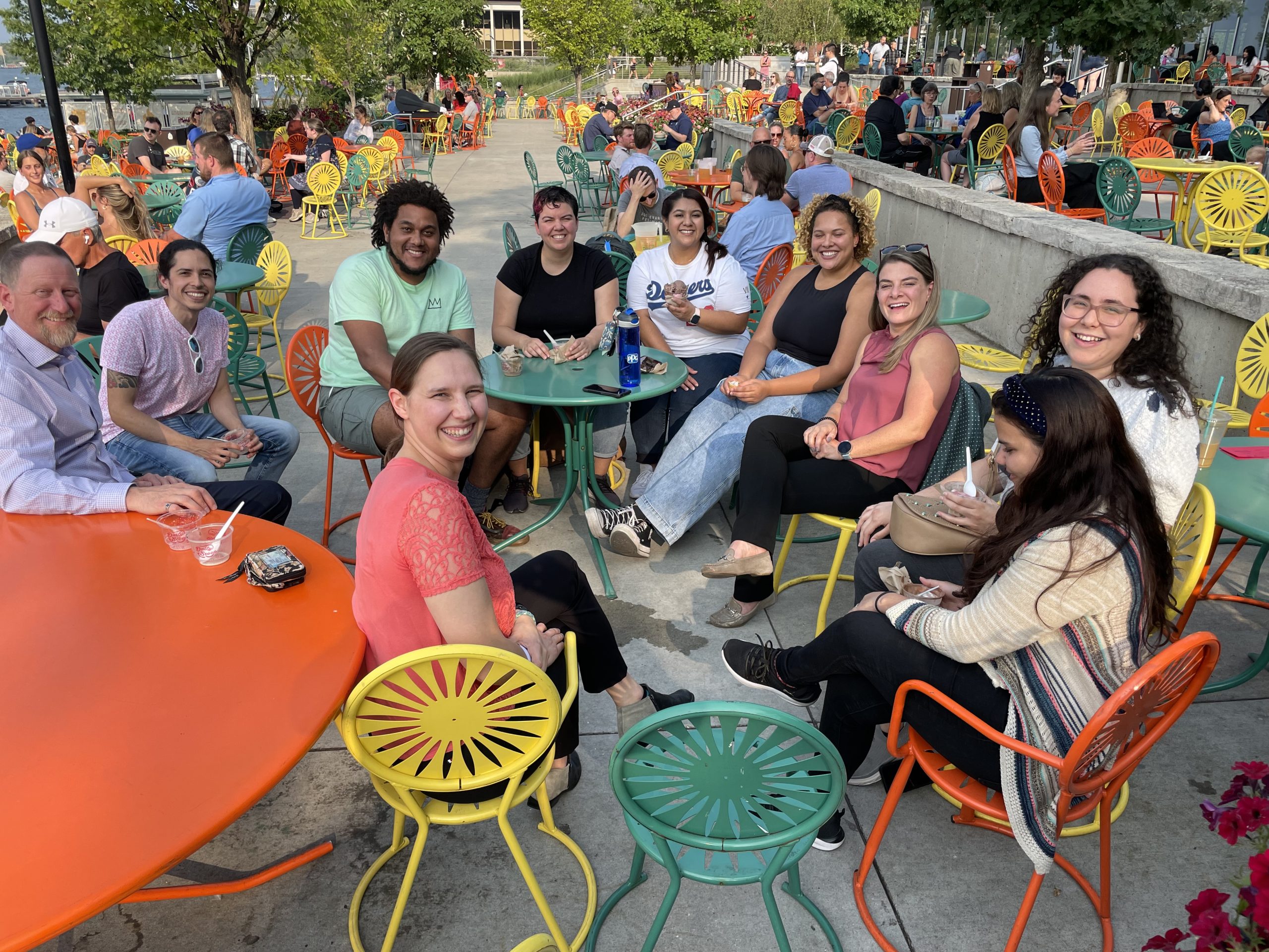 A group of people smile at the camera holding dishes of ice cream among colorful tables and chairs on the Memorial Union Terrace on a sunny summer day.