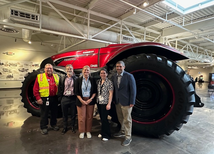 Five people stand in front of a large red Case IH tractor displayed indoors.