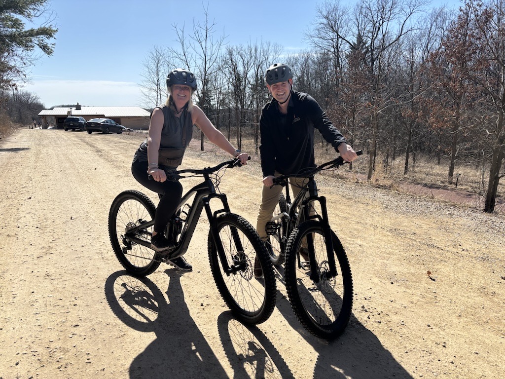 Two people ride on bikes on a gravel path.